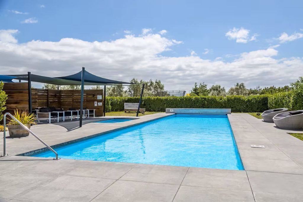 Piscina com toldo, espreguiçadeiras e cerca de madeira.