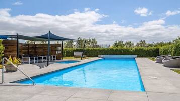 Piscina com toldo, espreguiçadeiras e cerca de madeira.