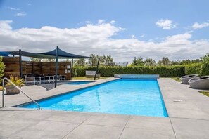 A swimming pool with a sunshade, lounge chairs, and a wooden fence.
