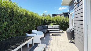 Eine Terrasse mit Gartenmöbeln, darunter eine Couch und Stühle, umgeben von viel Grün.