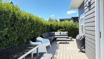 A deck with outdoor furniture, including a sofa and chairs, surrounded by greenery.
