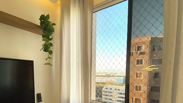 Ein Zimmer mit Fernseher, Pflanze, Fenster mit Blick auf Gebäude und Deckenleuchte.