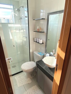 A bathroom with a glass shower enclosure, a toilet, a sink, and a mirror. - 2 bedroom apartment • With 1 vacancy • Near Galeão Airport (Duque de Caxias)