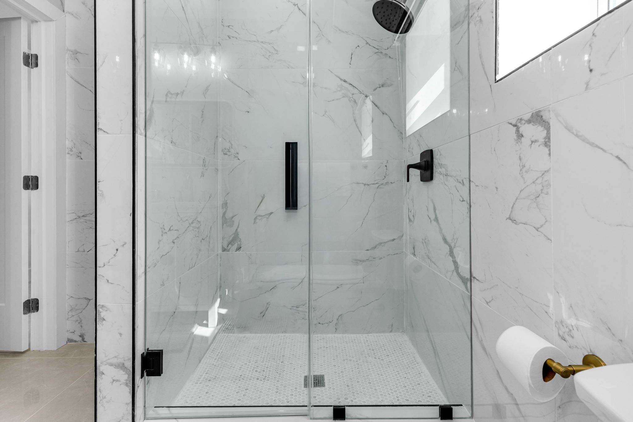 A modern bathroom with a glass-enclosed shower, marble walls, and a toilet paper holder.