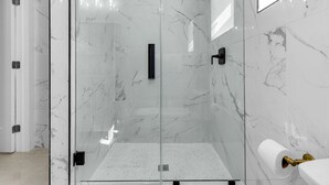 Un baño moderno con ducha envuelta en vidrio, paredes de mármol y un dispensador de papel higiénico.