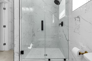 Un bagno moderno con doccia vetrata, pareti in marmo e porta carta igienica.