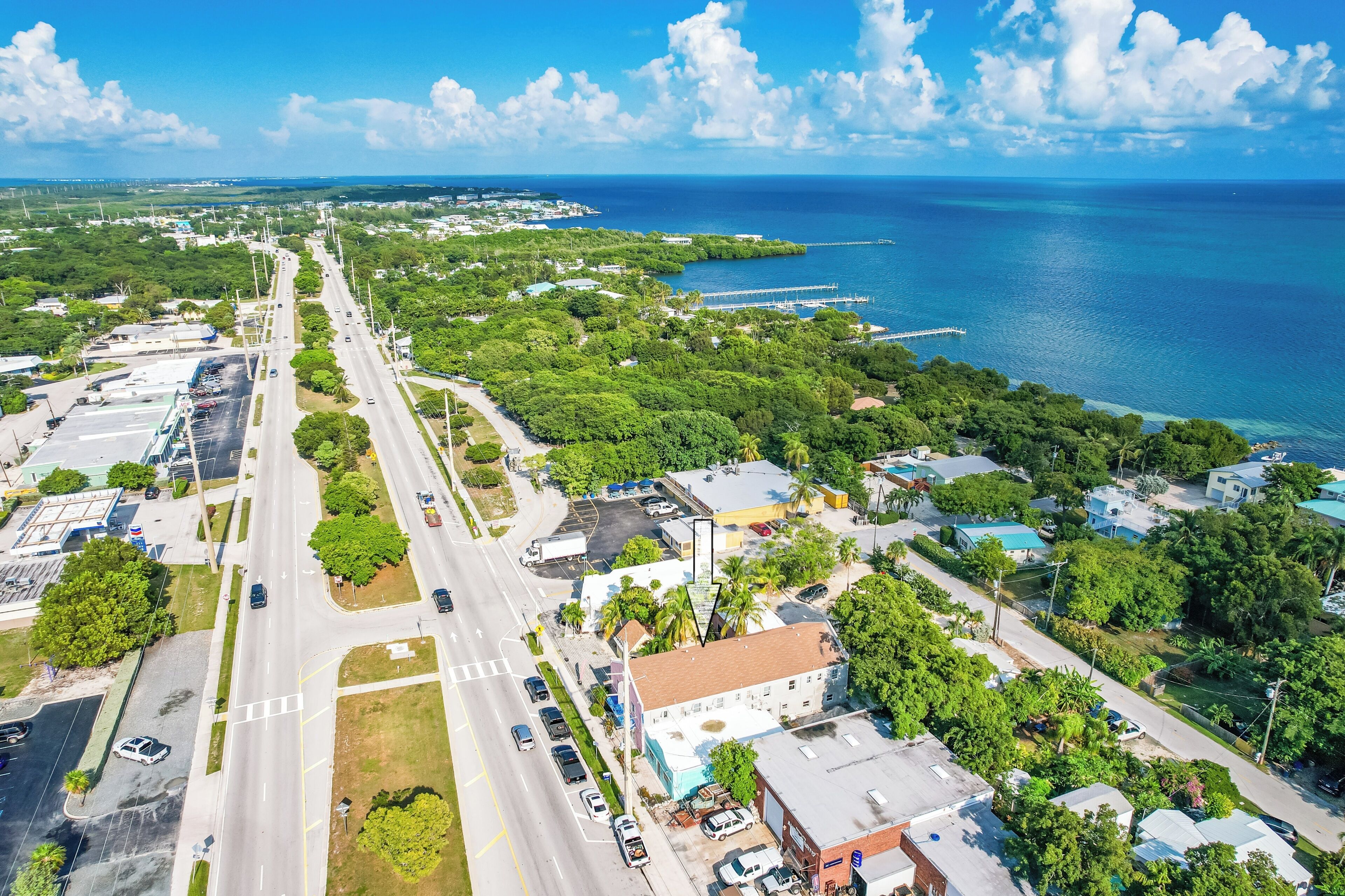 An aerial view of a coastal town with a main road, green spaces, and a marina.