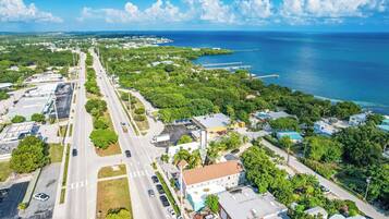 An aerial view of a coastal town with a main road, green spaces, and a marina.
