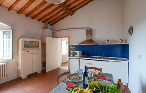 A kitchen with a tiled backsplash, a stove, a microwave, and a dining area with a table set for two. - Cozy apartment in Poggibonsi with swimming pool (Poggibonsi)