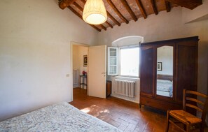 A bedroom with a wooden ceiling, a bed with a floral bedspread, a wooden wardrobe, and a window with a view. - Cozy apartment in Poggibonsi with swimming pool (Poggibonsi)