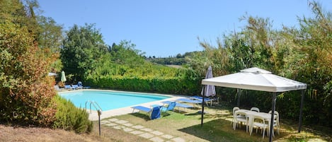 A swimming pool with lounge chairs and a covered seating area.