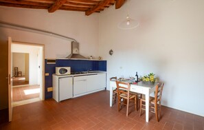 A compact kitchen with a white refrigerator, a stove, and a blue backsplash. There's a dining table with chairs and a hanging light fixture. - Cozy apartment in Poggibonsi with swimming pool (Poggibonsi)