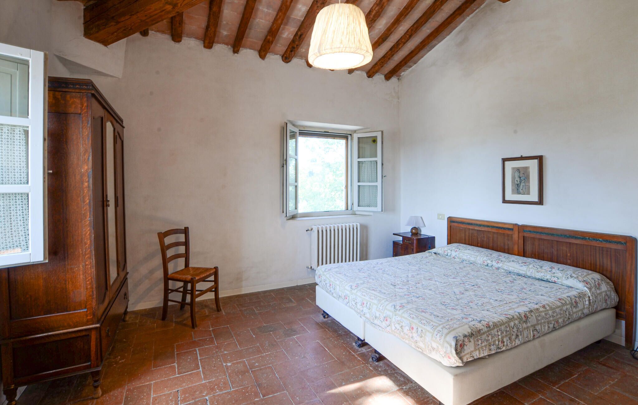 A bedroom with a bed, a chair, a window, a radiator, and a wooden wardrobe.