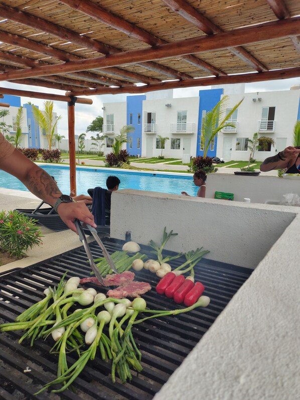 A poolside barbecue grill with various meats and vegetables being cooked.