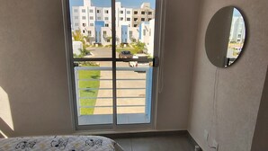 Een slaapkamer met een bed, een schuifdeur met glas en een rond spiegel, met uitzicht op gebouwen.