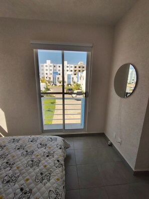 A bedroom with a bed, a sliding glass door, a round mirror, and a view of buildings outside. - CASA MARIEL ACAPULCO DIAMANTE 🌊🌴 POOL, GARDEN, BEACH, SUN, SAND, AND OCEAN (Acapulco de Juárez)