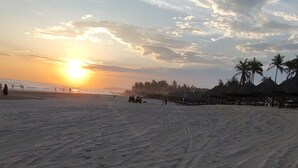 Een strand met sporen van banden en palmbomen in de verte.