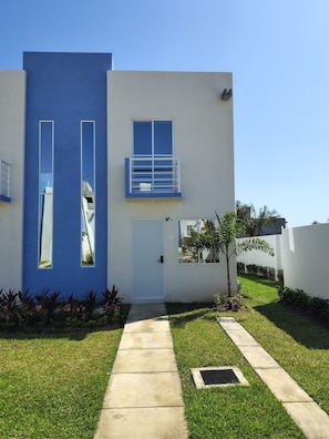A modern two-story house with a blue facade, a small balcony, and a well-maintained lawn.