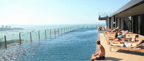 Une piscine à débordement située sur le toit, offrant une vue sur la mer et le paysage urbain.