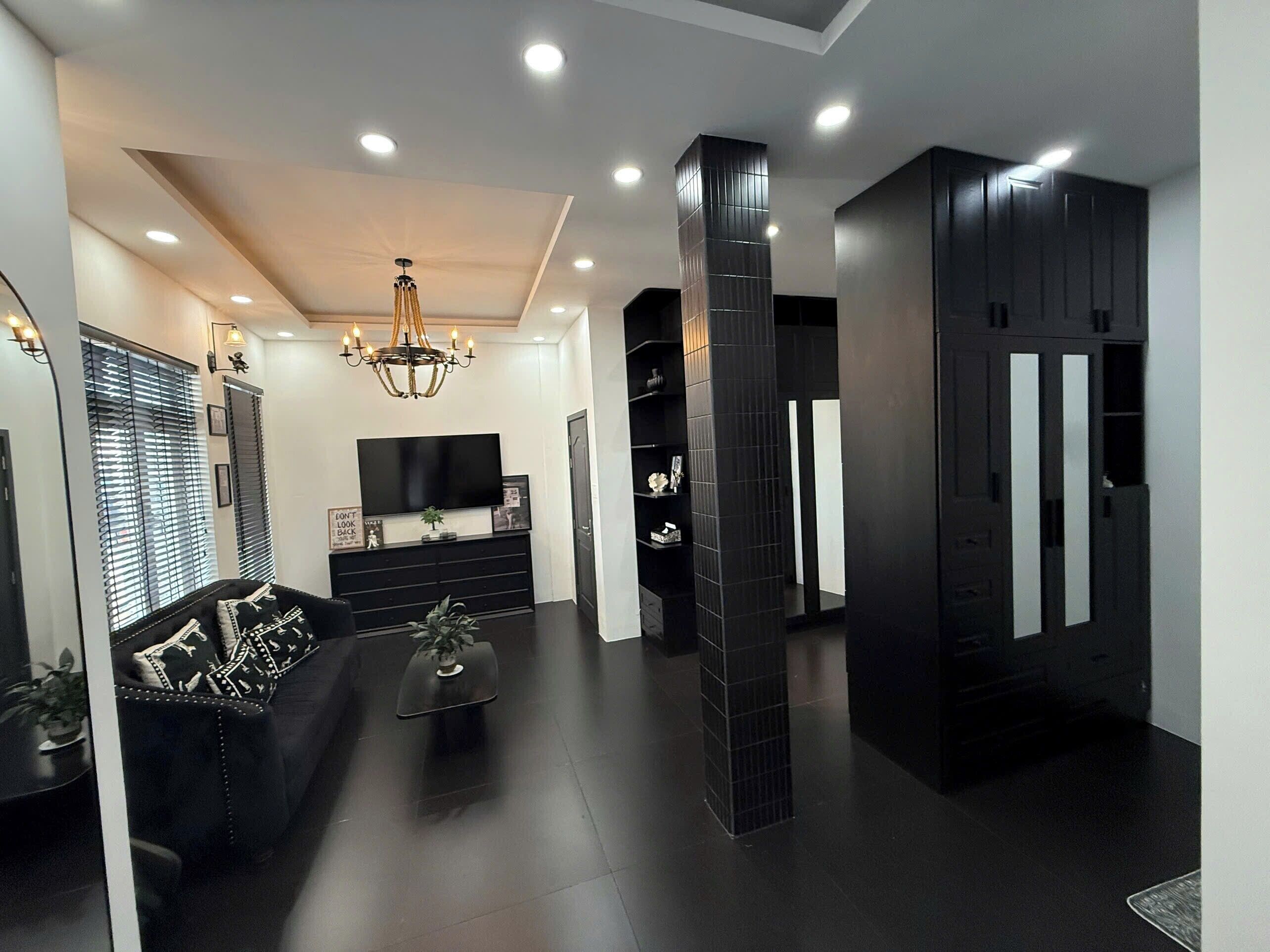 A modern living room with a black sofa, a TV, a chandelier, and a black entertainment unit.