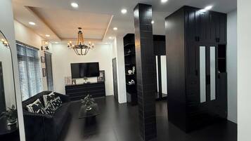 A modern living room with a black sofa, a TV, a chandelier, and a black entertainment unit.