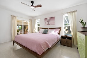 A bedroom with a bed, a nightstand, a dresser, a ceiling fan, and a window with curtains. - Unique Mid Century Pool Home 5 Miles To The Beach (Largo)