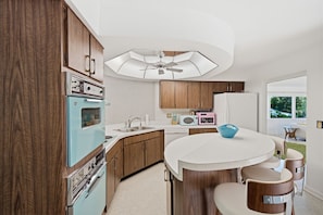 Een moderne keuken met een centraal eiland, houten keukenkastjes, een oven in vintage blauw en een plafondventilator.