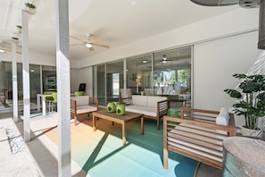 Een moderne woonkamer met een bank, salontafel en stoelen, een glazen deur die naar een balkon leidt, en een plafondventilator.