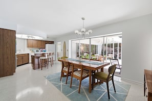 A modern kitchen with wooden cabinets, a dining area with a large table and chairs, and a sliding glass door leading to a patio. - Unique Mid Century Pool Home 5 Miles To The Beach (Largo)