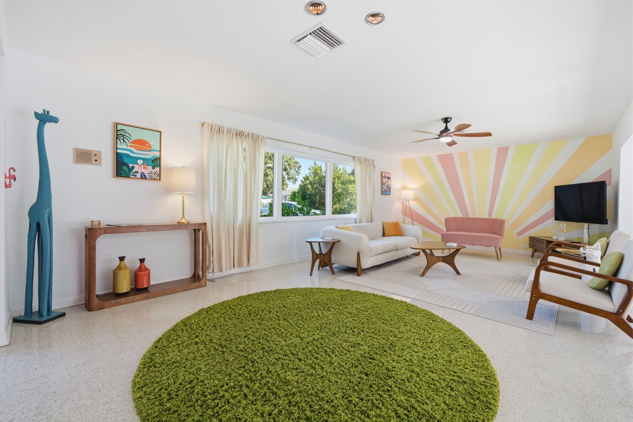 A living room with a white sofa, a pink armchair, a green rug, and a ceiling fan.