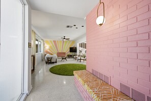 A hallway with a pink brick wall, a green carpet, and a bench with a patterned cushion. - Unique Mid Century Pool Home 5 Miles To The Beach (Largo)