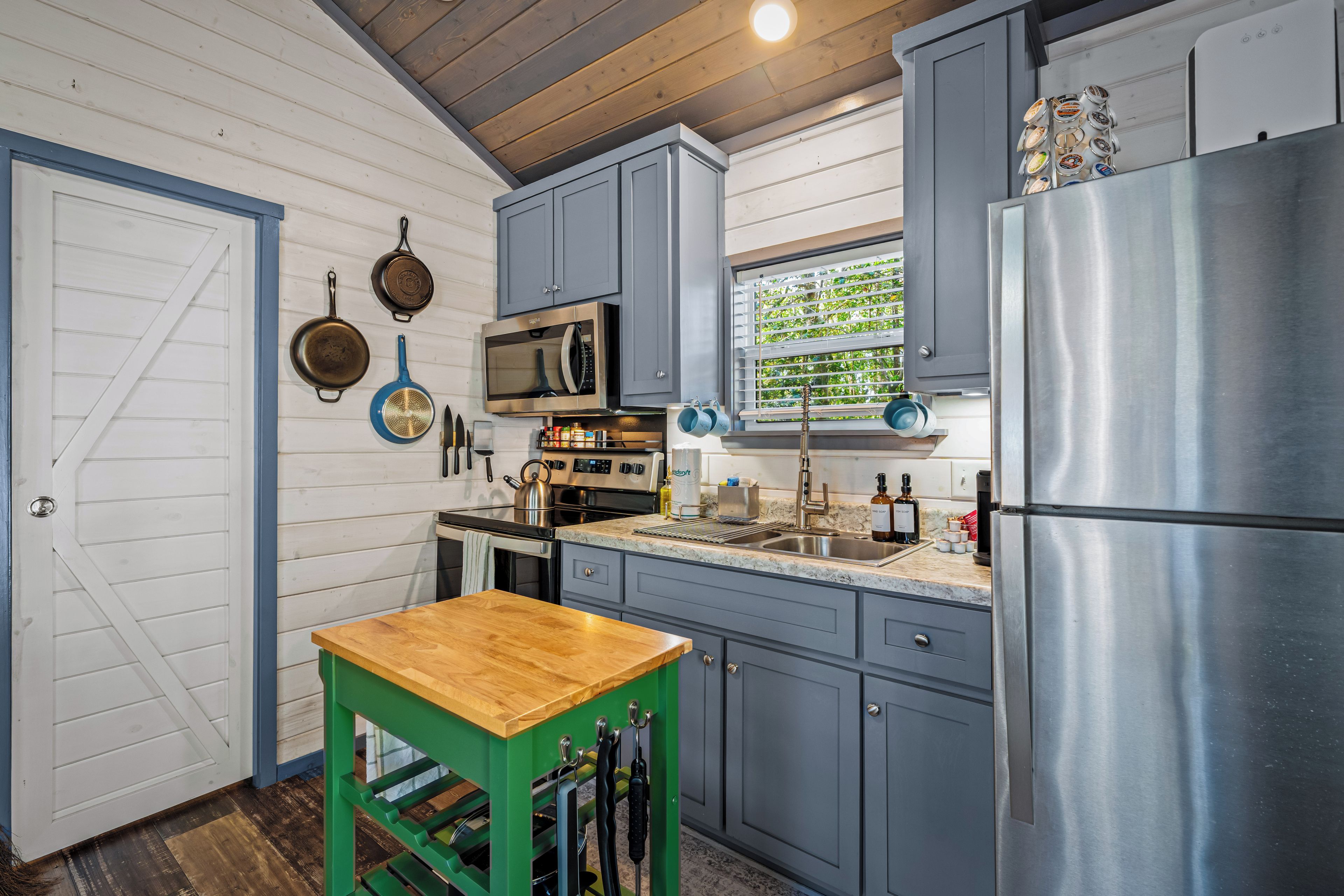 A kitchen with a wooden table, stainless steel appliances, and a window with blinds.