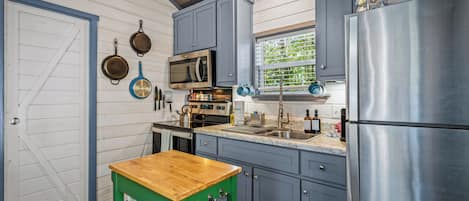 Una cocina con una mesa de madera, electrodomésticos de acero inoxidable y una ventana con persianas.