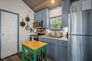 A kitchen with a wooden table, stainless steel appliances, and a window with blinds.