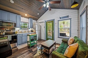 A compact kitchen with modern appliances, a dining area with a green sofa, and a view through a door.