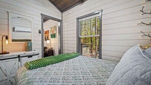 A bedroom with a bed, a dresser, a mirror, and a window with a view.