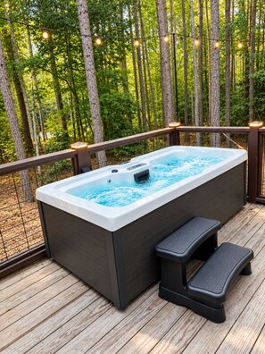 Een hottub op een houten terras met een leuning, omringd door bomen en sfeerverlichting.