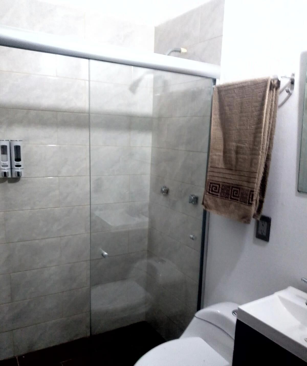 Un baño con cabina de ducha de vidrio, inodoro y lavamanos.