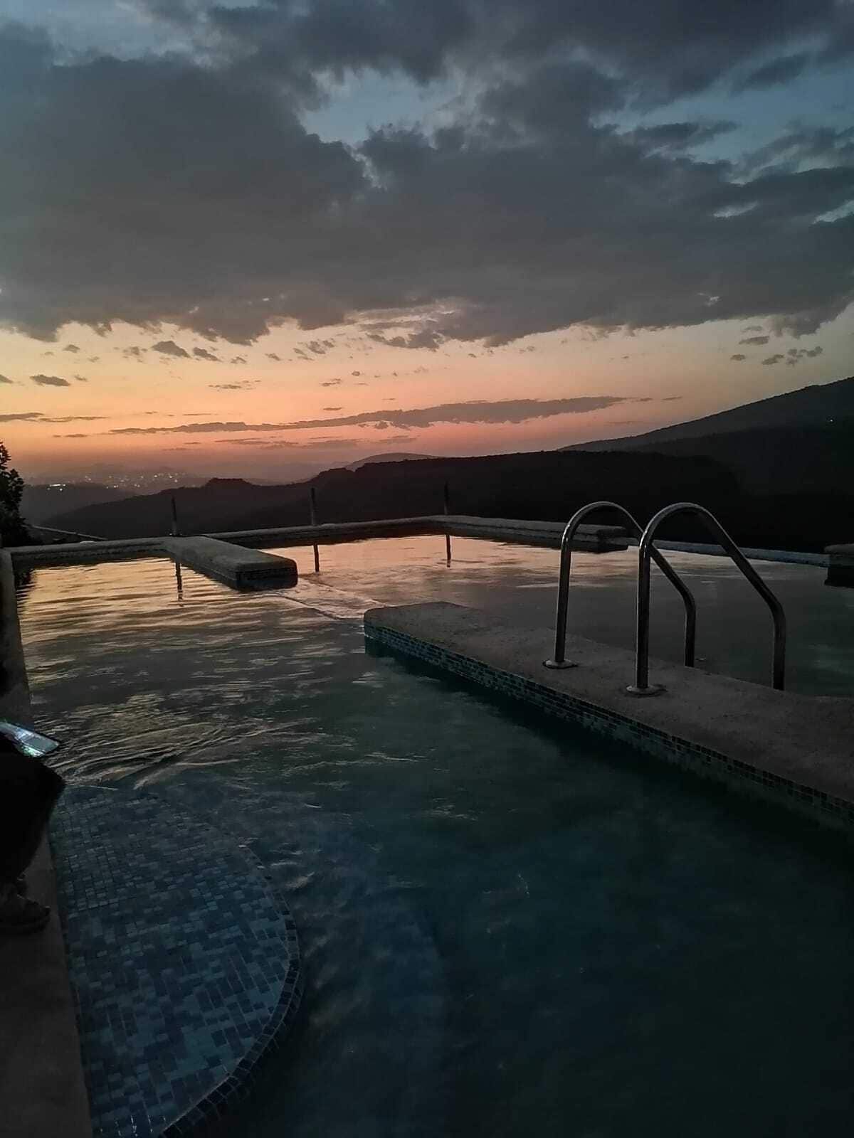 Une piscine à débordement offrant une vue sur un coucher de soleil se déclinant sur un paysage vallonné.