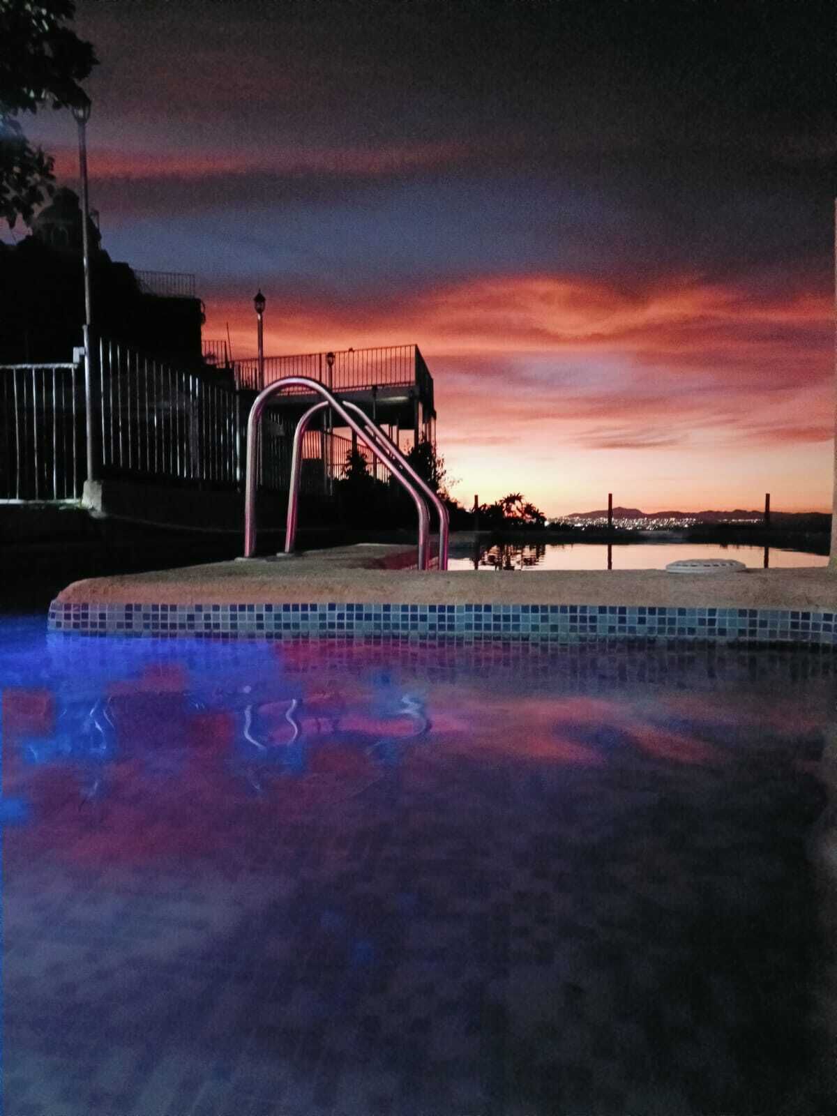 Una piscina con una escalera de metal y vistas a un horizonte urbano al atardecer.