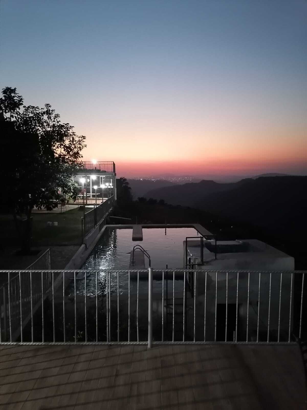 Una piscina con vistas a la puesta de sol y colinas al fondo.