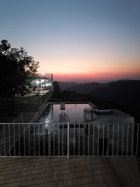 A swimming pool with a view of the sunset and distant hills.