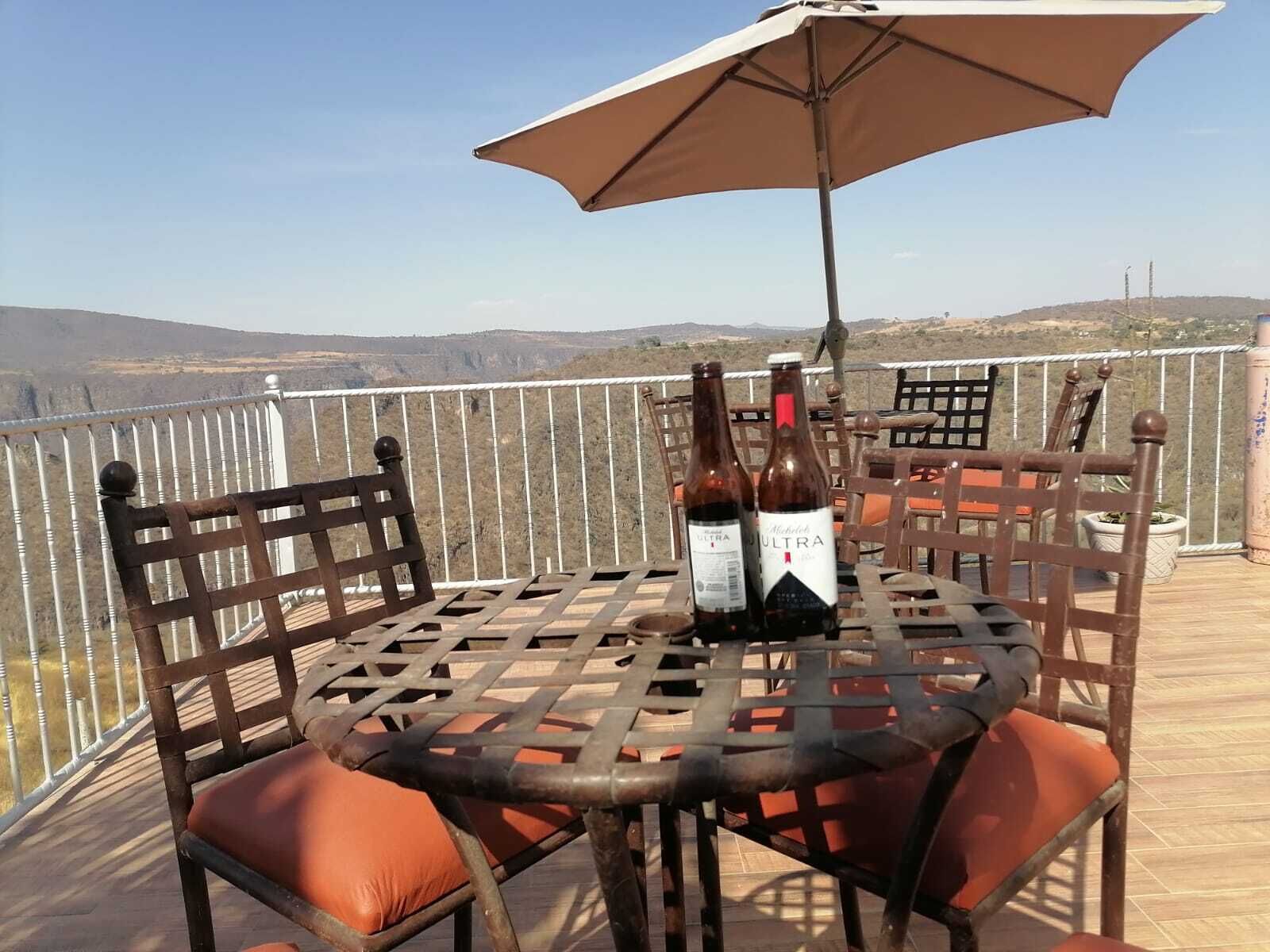 Une table avec deux bouteilles de vin, une chaise en métal et un grand parasol sur un balcon offrant une vue sur le paysage.