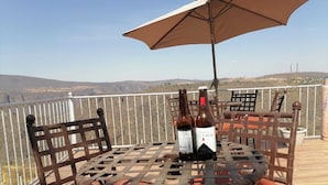 Een tafel met twee flessen wijn, een metalen stoel en een grote parasol op een balkon met uitzicht op het landschap.