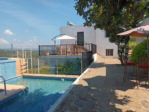 Una piscina con borde de azulejos, un área de estar cubierta con sillas y vistas al paisaje.