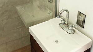 Een badkamer met een glazen douchecabine, een witte wastafel met één kraan en een spiegel boven de wastafel.