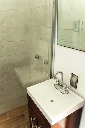 A bathroom with a glass shower enclosure, a white sink with a single faucet, and a mirror above the sink. - Vrbo Property (Tonalá)