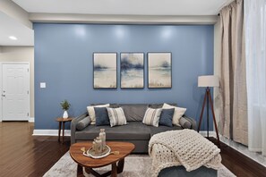 Ein Wohnzimmer mit einem grauen Sofa, drei Wandbildern, einer Stehlampe und einem Couchtisch mit Dekoration.