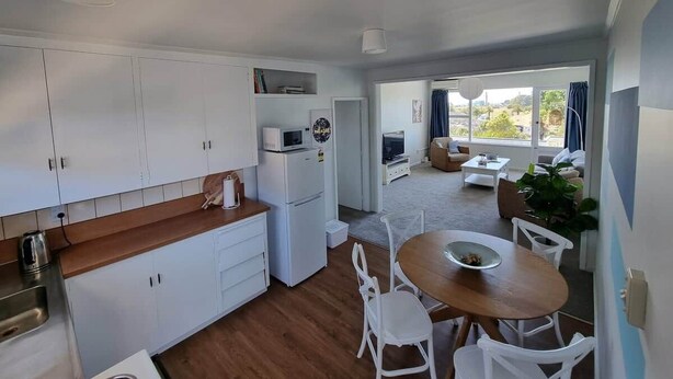 A compact kitchen with white cabinets, a microwave, and a refrigerator. There is a dining area with a wooden table and white chairs.