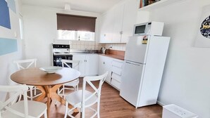 A modern kitchen with white cabinetry, a wooden dining table, and white chairs. - Bay Getaway 2 Bedroom apartment (Timaru)